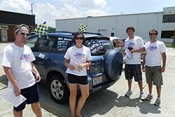 Four people posing alongside an SUV with flags and writing on it