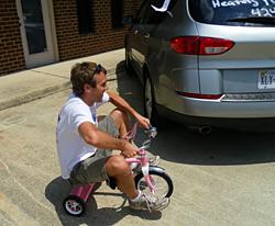 Adult man biking on child's pink tricycle