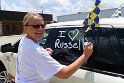 Blonde woman writing Russell's on SUV window with removable marker 