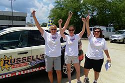 Three women with their hands up in front of Russell's SUV