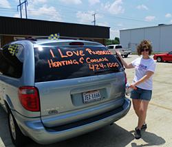 Woman showing off writing that reads, "I love Russell's" in erasable marker on back of silver mini-van 