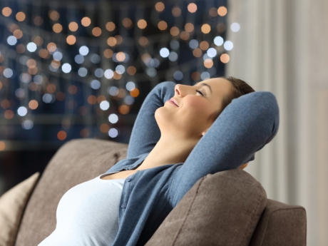 Young woman with brown hair relaxing on tan couch with winter lights in background