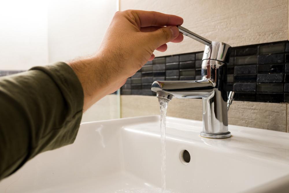 Man turning on bathroom tap with low water pressure