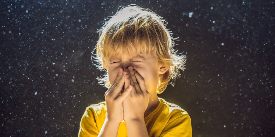 Little kid in a room full of dust particles, covering his nose