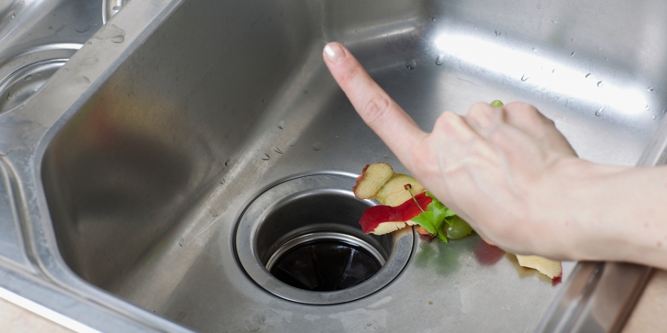 hand holding one finger up to a garbage disposal with peels in it